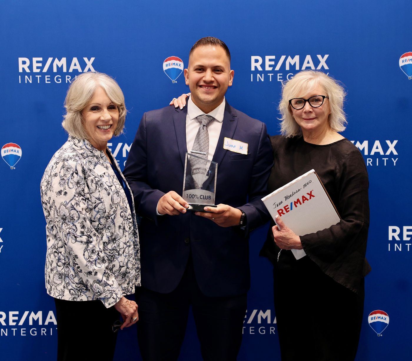 Juan Mendoza holding a RE/MAX 100% Club award with his RE/MAX Integrity manager and managing broker